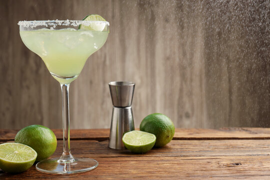 Refreshing margarita cocktail in glass, limes and jigger on wooden table, closeup. Space for text