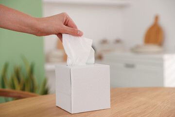 Woman taking paper tissue out of box at wooden table indoors, closeup. Space for text