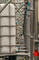 A long perspective corridor of metal scaffolding trusses and white water ballast tanks stands at an outdoor festival stage setup. © Dmitry