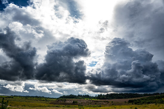Heavy dark storm clouds gather dramatically over rolling rural fields and a distant forest line.