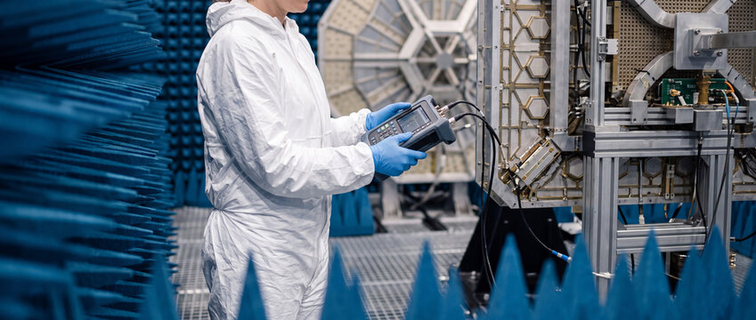 Technician using spectrum analyzer to test satellite antenna in anechoic chamber lab