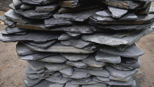 Close up shot with slow camera movement across a stack of natural slate stones. The video reveals the rough texture, layers, and grey tones of the rock, suitable for construction or garden design