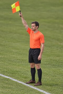 Assistant referee raising an orange and yellow flag during a soccer match