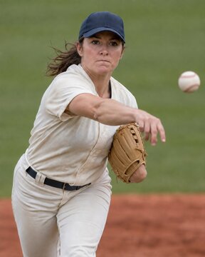 Female baseball pitcher in uniform throwing a ball on the mound, vertical close-up