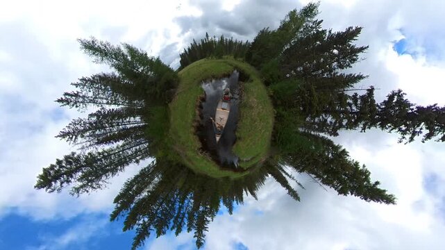 Wide angle globe like view of two people paddling a canoe along a narrow park stream
