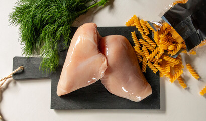 Raw chicken breast with fusilli pasta and fresh dill on a black slate board © Ivika