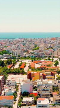 Vertical video. Alexandroupolis, Greece. Panoramic Drone footage over the central city and Thracian Sea coast, white apartment blocks and terracotta rooftops stretching toward a busy commercial port,