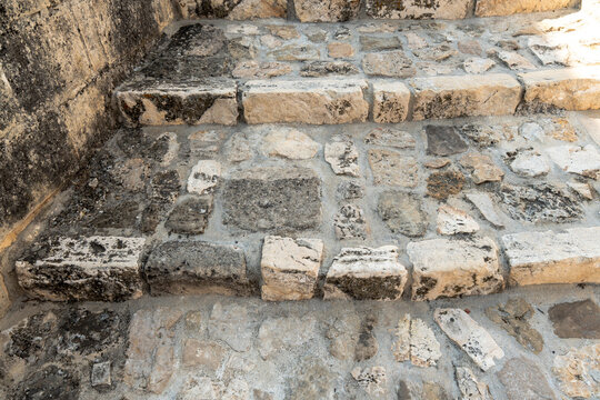 Worn limestone steps of an ancient staircase with irregular stone blocks and dark weathering in a historic Mediterranean town, close view of old masonry stairs, natural stone texture background, conc