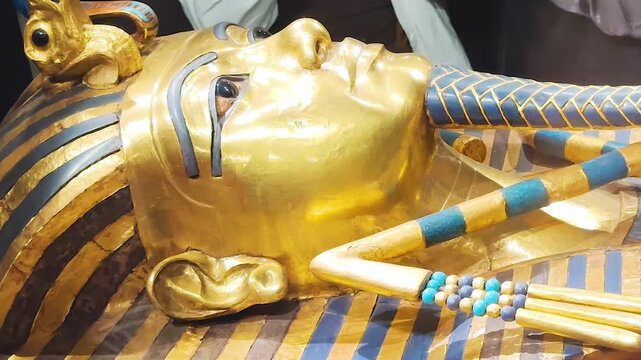 Tutankhamun's golden burial mask featuring blue inlays, a headdress, and arms crossed over the chest holding a crook and flail.