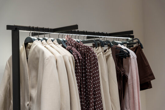 Fashion garments hang on retail rack inside modern boutique, creating tidy clothing display. Neutral jackets and patterned tops suggest refined shopping space with polished, minimalist mood.