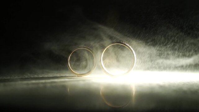 Elegant wedding rings resting on a reflective surface, surrounded by soft mist and dramatic lighting, capturing the essence of love and commitment in a romantic atmosphere