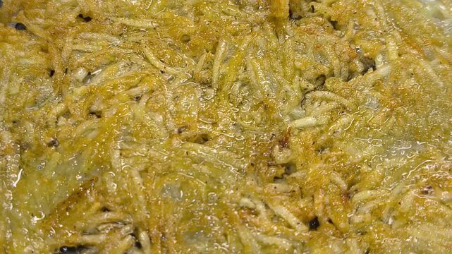 Large grated potato fritter cooking in a frying pan. Hot oil bubbles around the potato pancake as a golden crispy crust forms during frying. Homemade potato pancake made from coarsely grated potatoes.