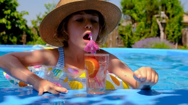 A child is drinking a cocktail by the pool. Selective focus.