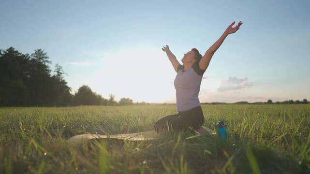 A woman practices yoga in a field during sunset. The woman sits gracefully, exuding calmness and focus in the serene, natural setting of grass.