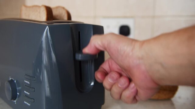 A hand turning on the electric plug switch and pressing the toaster on lever to make toasts. A domestic appliance, energy use concept.