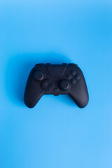 Vertical flat lay of a black wireless gamepad controller on a blue background. Perfect for mobile gaming ads, esports, and social media.  © wibiwisnu
