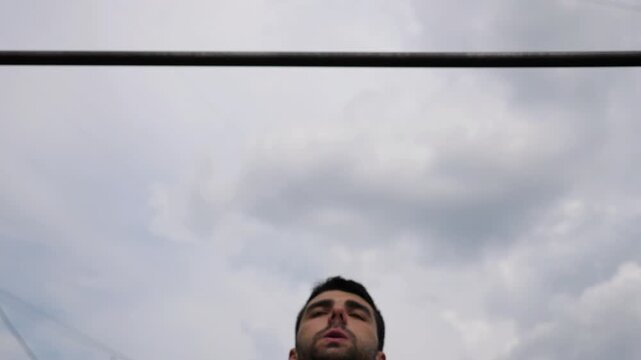 Sportsman performing intense pull-up workout, showcasing muscular strength and determination, with a focus on upper body engagement against a cloudy sky backdrop, illustrating fitness progression