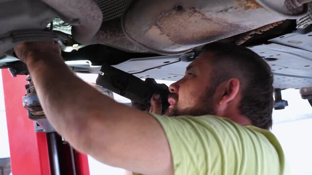 Skilled mechanic performing detailed automotive repair under vehicle, showcasing precision work with tools in a well-equipped garage, highlighting intricate process of vehicle maintenance and service