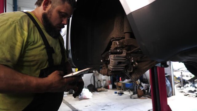 Skilled automotive mechanic with beard, focused on removing brake caliper from vehicle in well-lit garage, showcasing detailed craftsmanship and precision during the repair process