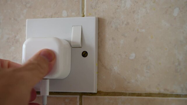 A hand putting a plug into a electric wall socket and pressing the power on button. A electricity use concept.