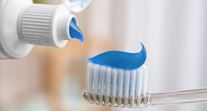Toothpaste on toothbrush and tube against blurred background, closeup. Banner design
