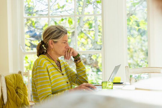 adult woman sitting at table in light filled room using mobile phone with laptop on table