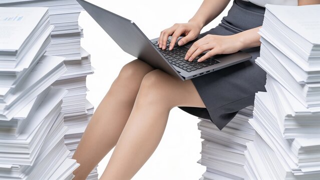 Work on laptop surrounded by piles of paper documents in an office setting
