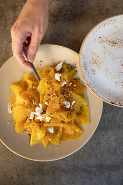 overhead shot of hand with spoon reaching into plate of golden beets with cheese for serving family style dining