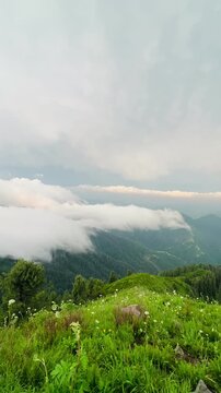White clouds rolling over green mountain ridge in valley