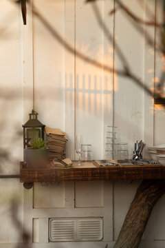 stack of restaurant items - glasses, napkins, silverware, outdoors against white wall with dappled light shadows