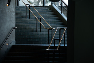Modern architectural staircase with tiled steps and metallic handrails in a dim interior space © Tom Harwood