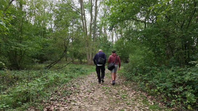 Two hikers walk along a leaf-strewn forest path