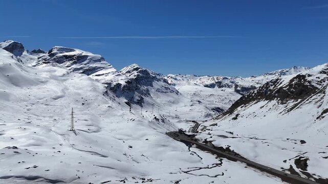 winding mountain road threads snowbound valley pylons trace route toward distant jagged peaks julier pass mountain crossing graubunden switzerland high altitude european alps