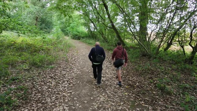 Two people walk slowly through a leafy forest path