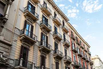 Fototapeta premium Historic Liberty style apartment building with ornate balconies and stone decorations seen from below against a blue sky with white clouds, low angle view of an elegant European facade in summer, con