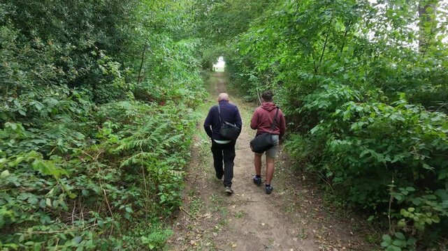 Two hikers walk along a narrow forest path