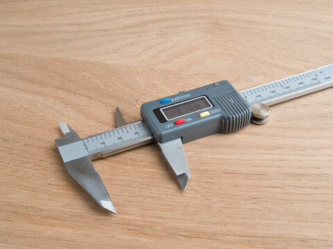 Digital Caliper on Wooden Surface - A stainless steel digital caliper with LCD display resting on a light wood surface, showing inch and mm scales.