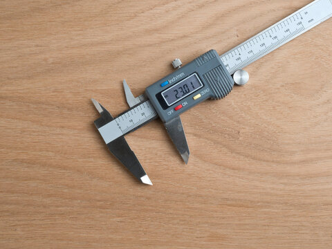 Digital Caliper on Wooden Surface - A stainless steel digital caliper with LCD display resting on a light wood surface, showing inch and mm scales.