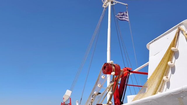 View of a traditional Greek fishing boat adorned with colorful fishing nets and a Greek flag waving in the breeze on the island of Aegina, Greece, beneath a clear blue summer sky.