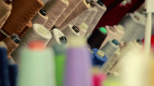 Colorful thread spools closeup textile factory. Yarn cone rack garment workshop.