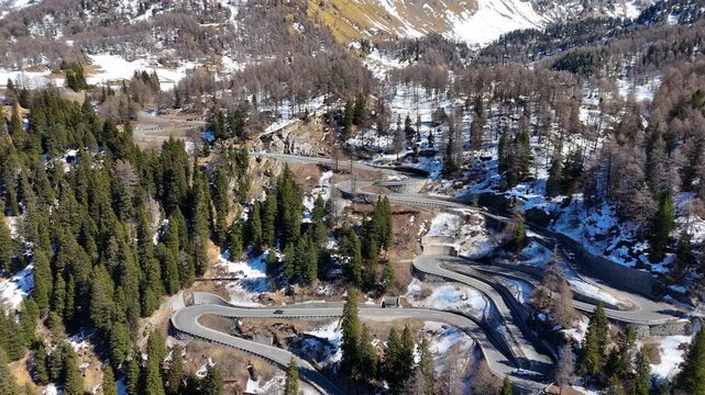 rugged snow dusted peak rises above switchback road hairpin bends winding pine forest truck car descend malojaschlange mountain pass graubunden switzerland val bregaglia