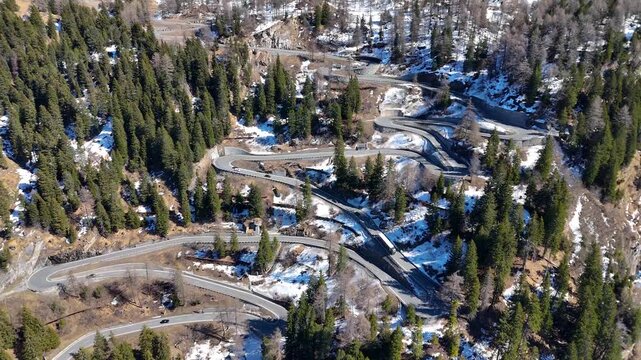 dense pine forest blankets switchback road complex winding mountainside snow patches scattered hairpin bends malojaschlange mountain pass graubunden switzerland val bregaglia