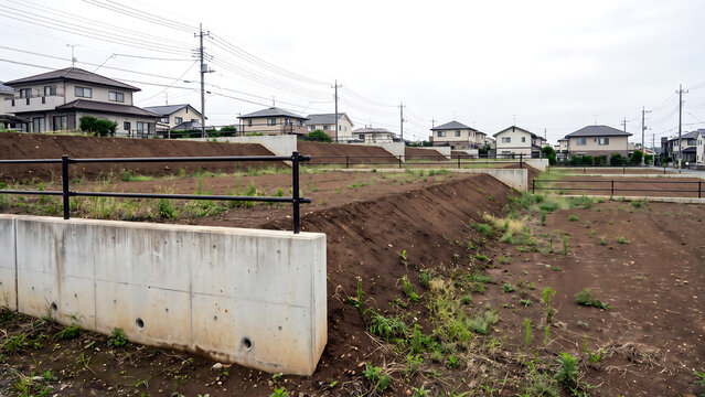 戸建て住宅を背景にした段差のある造成中の宅地区画とコンクリート擁壁・手すり柵