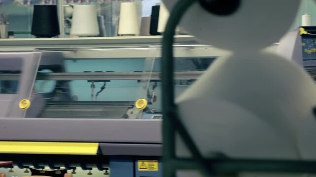 Automated knitting machines working textile plant. Camera pan white yarn spools.