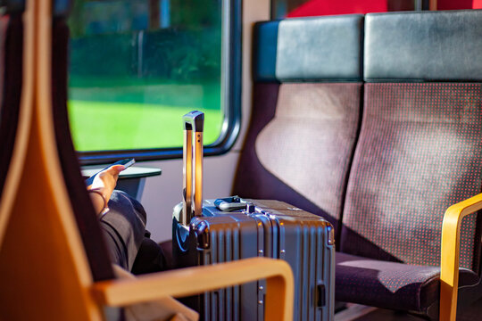 Traveler sitting with luggage and smartphone inside comfortable passenger train carriage near window with copy space