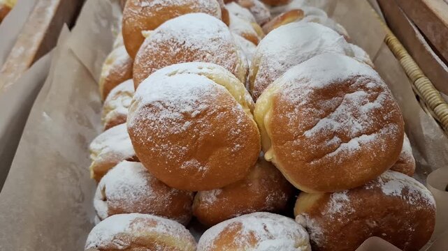 large pile of fresh golden berliner donuts sprinkled with powdered sugar in a wicker basket, traditional sweet bakery products and delicious dessert pastry concept.