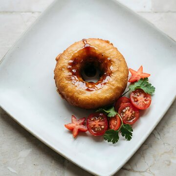 Plato cuadrado con una rosquilla o aperitivo frito decorado con tomates cherry y hierbas frescas