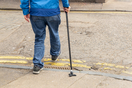 Person using walking cane stepping off kerb onto road