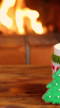 Mugs in knitted woolen covers with a Christmas ornament are placed in front of the fireplace. Xmas decorations on a wooden table in front of a flame burning in the fireplace. Vertical video