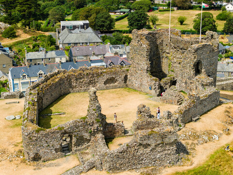 Medieval castle ruins showing stone outer walls, inner bailey and keep towers, Welsh flag flying above historic fortification on sunny day